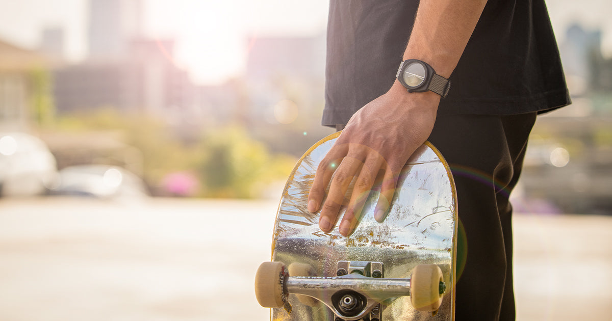 Skateboarder wearing a Nixon watch and holding his skateboard